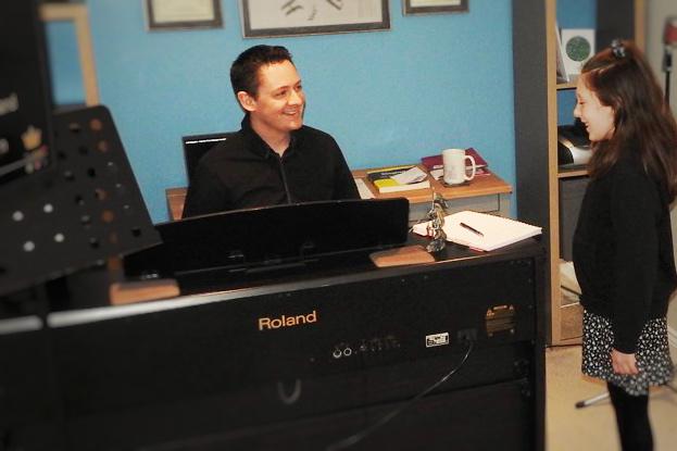 Christopher Williams : Vocal Teacher in South Wales sitting behind a piano teching a young girl how to sing